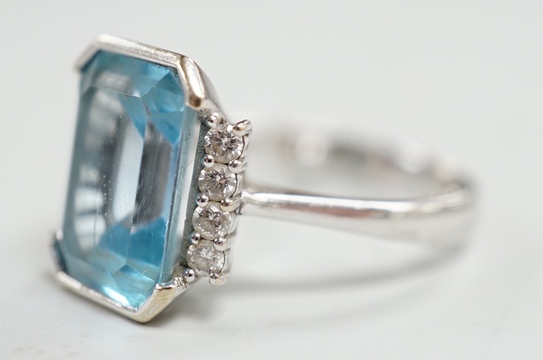 A 750 white metal and emerald cut blue topaz set dress ring, with diamond chip set borders, size O, gross weight 7.8 grams.